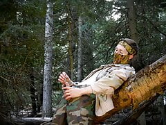 Soldier sounding his hung cock in the wilderness near a fallen tree.