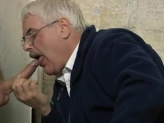 Grey old moustached man giving blowjob through glory hole