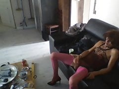 Sissy in pink fishnet has fun with dildo on the couch