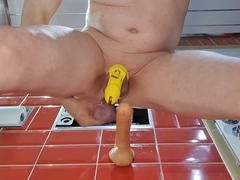 Elderly guy in chastity engaging with a dildo in the bathroom